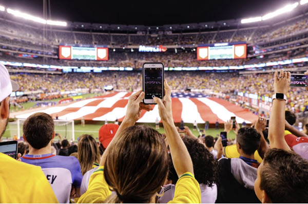 Redes sociales en el fútbol, mujer sostiene un smartphone en la gradas de un estadio 